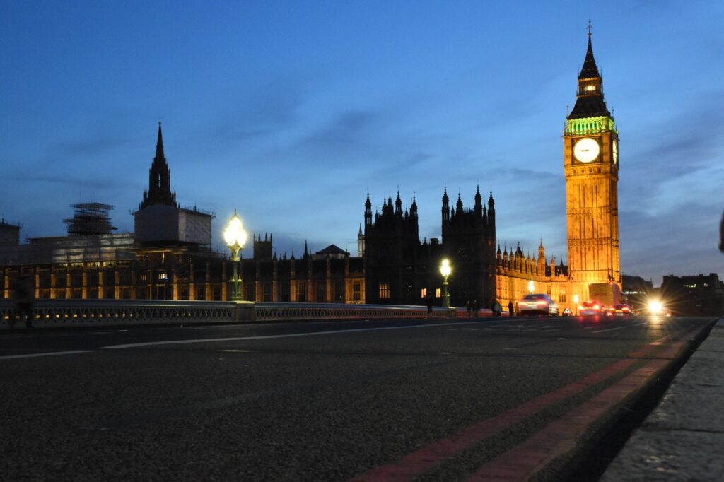  O Big Ben e a rua ao redor dele em Londres aparecem na imagem. Na foto é possível notar que é início de noite. Também há alguns automóveis perto do Big Ben. 