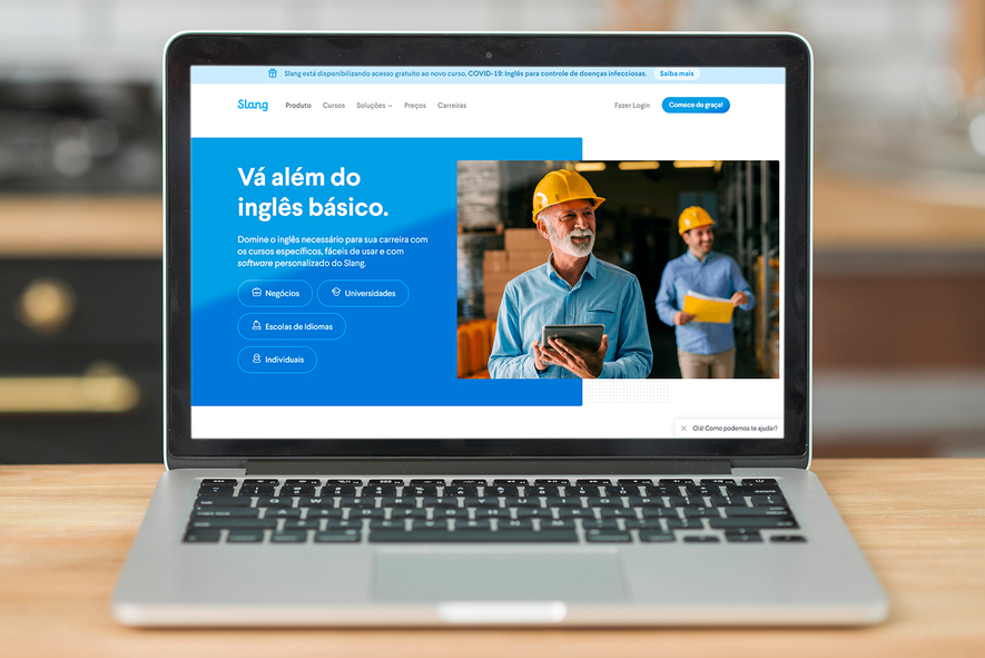 La imagen muestra una laptop abierta sobre una mesa de madera. En la pantalla se puede ver la página de inicio de Slang.